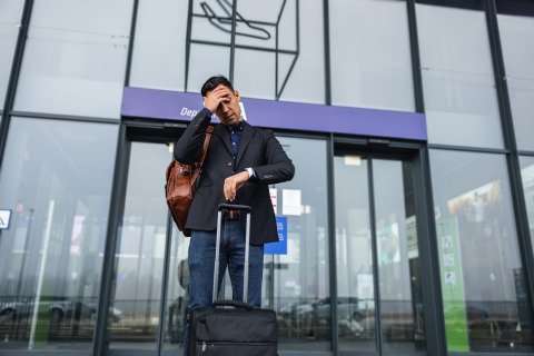 A man checking his watch outside an airport having missed his flight.